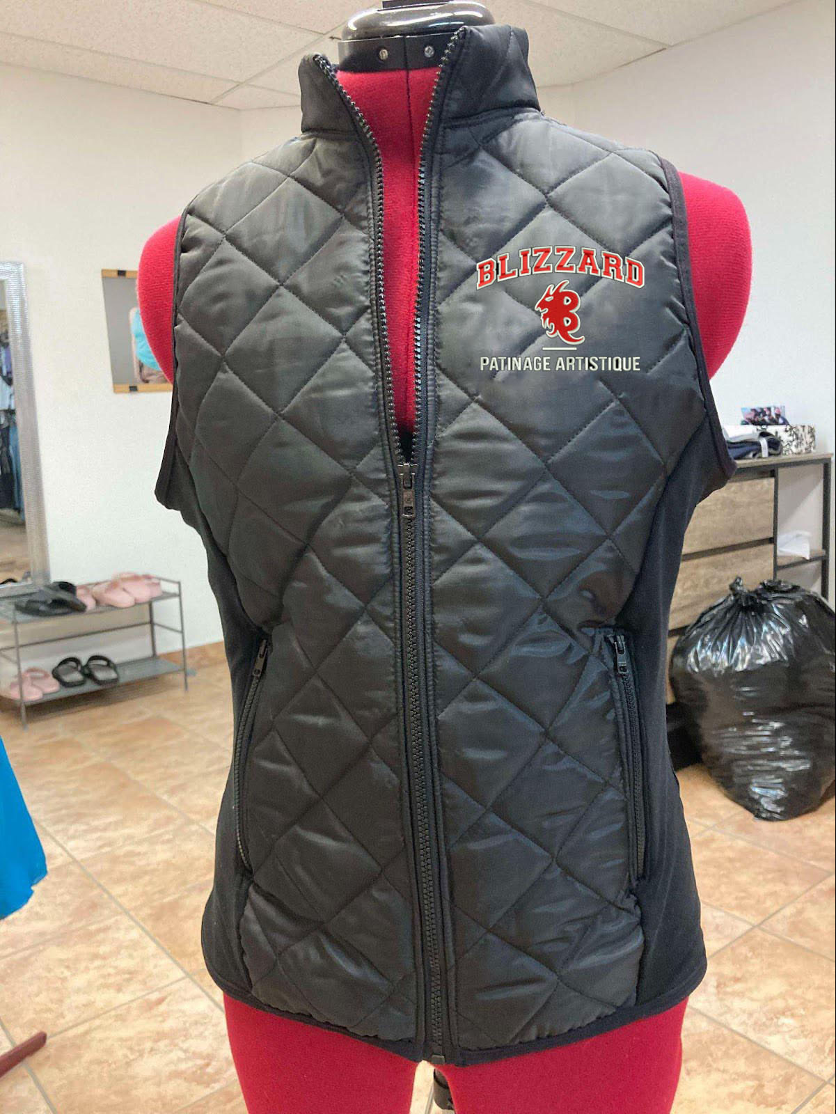 Veste sans manche avec poches à fermetures éclaires fait de tissu matelassé semi-imperméable et de supplex. Identification (broderie) du Blizzard Patinage Artistique en broderie au coeur et de Patinage Canada en petit au dos.